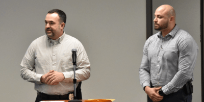 Detectives Josh Payne y Niko Rivera hablando en un podio.