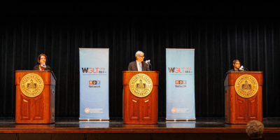 Tres concejales hablando en un escenario, cada uno en un podio.