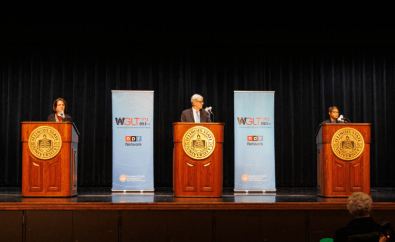 Tres concejales hablando en un escenario, cada uno en un podio.