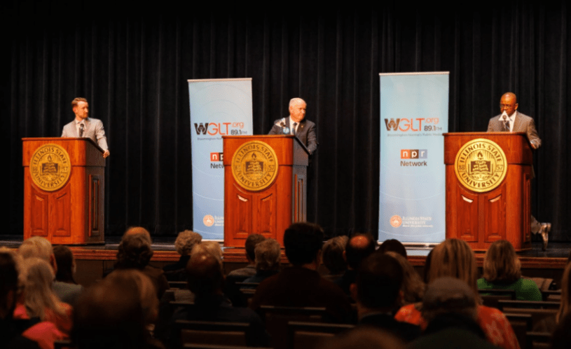 Tres candidatos hablando sobre un escenario, cada uno frente a un podio.