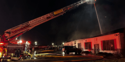 Camión de bomberos disparando agua sobre un local comercial durante la noche.