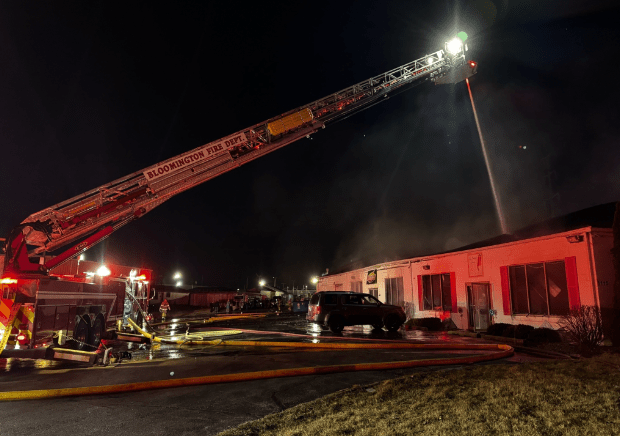 Camión de bomberos disparando agua sobre un local comercial durante la noche.