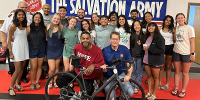 Grupo de ciclistas frente al letrero de Salvation Army y detras de una bicicleta.