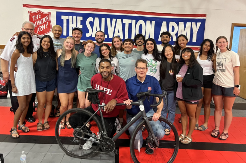 Grupo de ciclistas frente al letrero de Salvation Army y detras de una bicicleta.