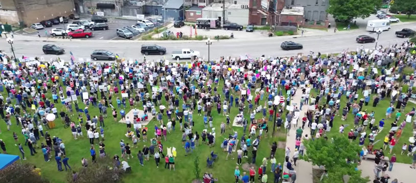 Carros circulando por una avenida y mucha gente observandolos y gritando consignas.