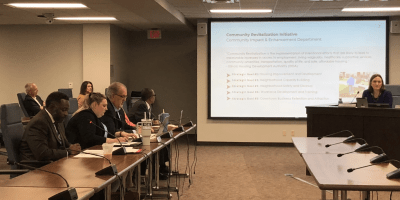 Miembros del Concejo Municipal de Bloomington sentados en una sala de reuniones, con computadoras portátiles y micrófonos sobre la mesa.