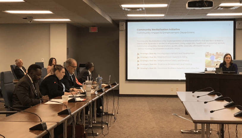 Miembros del Concejo Municipal de Bloomington sentados en una sala de reuniones, con computadoras portátiles y micrófonos sobre la mesa.