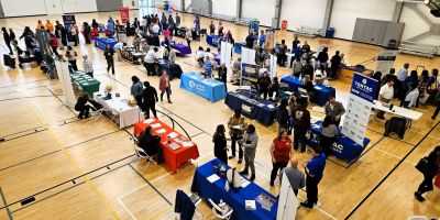 Vista aérea del gimnasio del YMCA con mesas de empresas y personas interactuando en la feria de empleo.