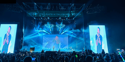 Público asistiendo a un concierto del festival Tailgate N’ Tallboys en Bloomington en 2024, con escenario iluminado y ambiente festivo.