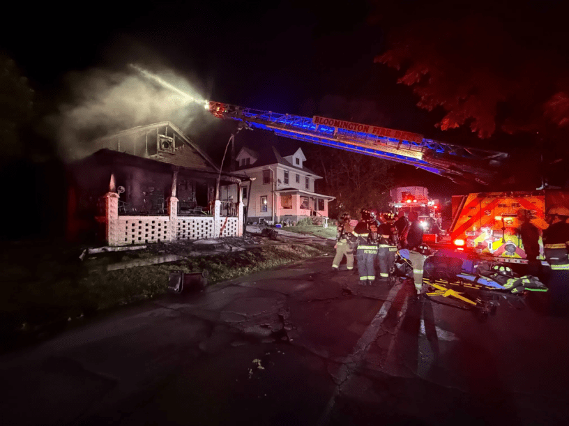 Bomberos operando el camión que tira agua sobre la casa medio destrozada.