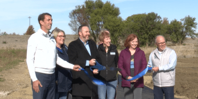 Jim Jacobs corta una cinta frente a un estanque y campo abierto durante una conferencia de prensa.