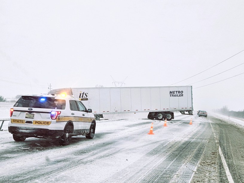 Camion accidentado en la carretera y un carro de la policia estatal parado al lado.