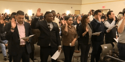 Grupo de nuevos ciudadanos levantan la mano derecha durante la ceremonia de naturalización en Peoria.