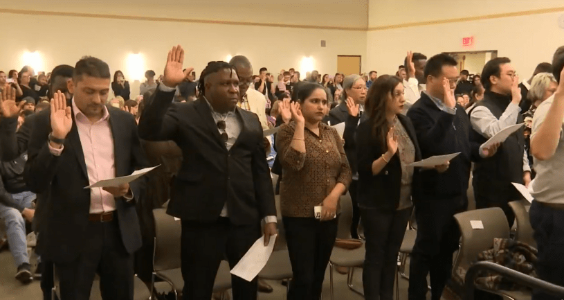 Grupo de nuevos ciudadanos levantan la mano derecha durante la ceremonia de naturalización en Peoria.