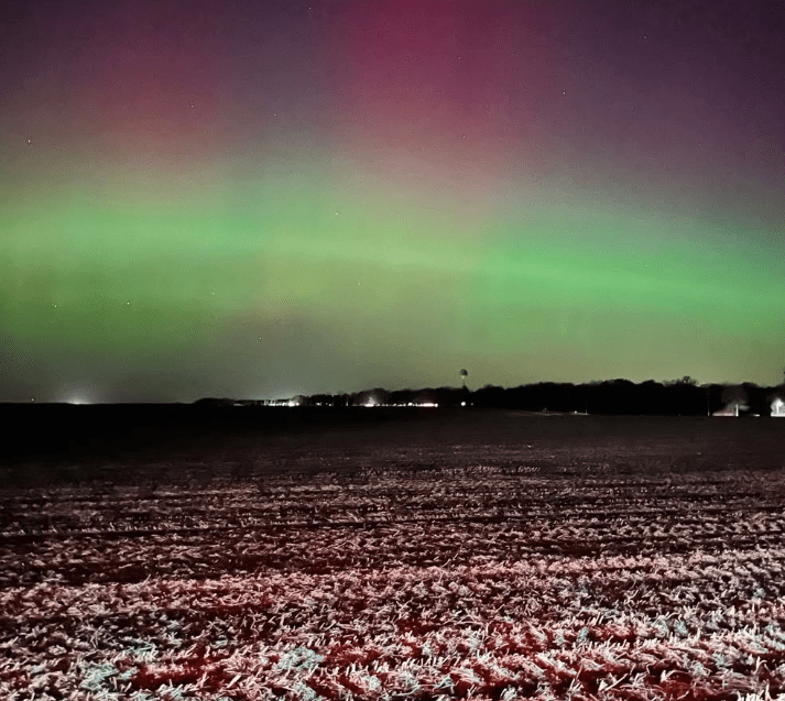 Cielo nocturno con auroras boreales visibles en tonos verdes y rosados sobre un área rural en Towanda, Illinois.