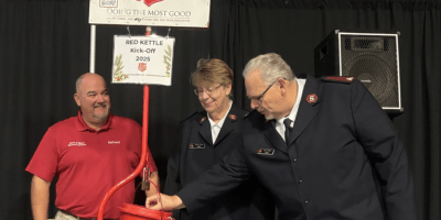 Dan Leisher, con uniforme de Salvation Army, poniendo una moneda en un contenedor rojo.