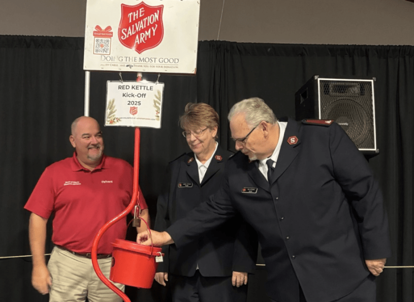 Dan Leisher, con uniforme de Salvation Army, poniendo una moneda en un contenedor rojo.