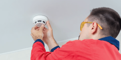 Un hombre instalando una alarma contraincendios en el techo.