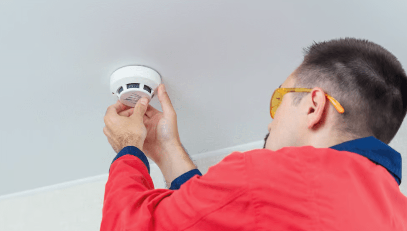 Un hombre instalando una alarma contraincendios en el techo.