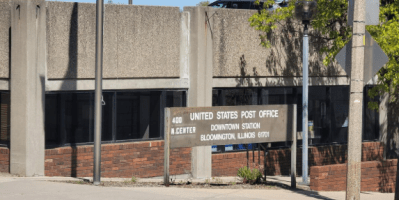 Puerta de la oficina postal del centro de Bloomington con un aviso de cierre y direcciones a otras sucursales.