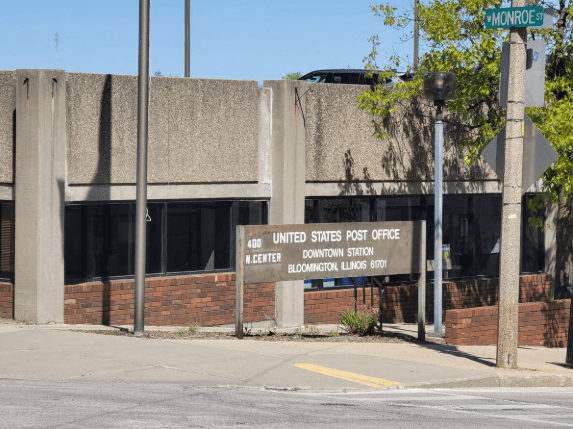 Puerta de la oficina postal del centro de Bloomington con un aviso de cierre y direcciones a otras sucursales.