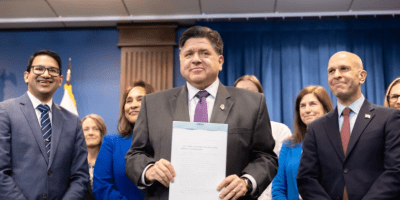 Gobernador de Illinois JB Pritzker posando para la foto, sosteniendo el documento firmado.