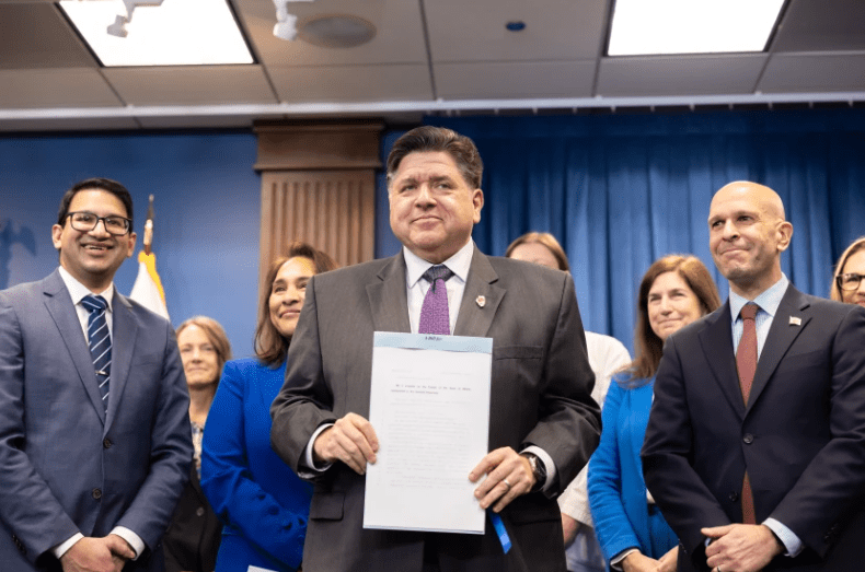 Gobernador de Illinois JB Pritzker posando para la foto, sosteniendo el documento firmado.