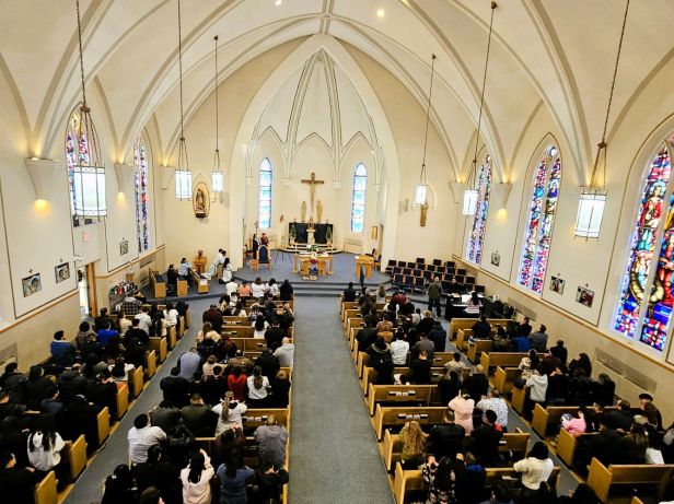 Toma general de la iglesia llena de gente en las bancas y el padre en el altar.