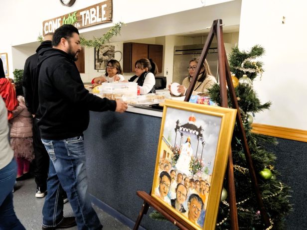 3 mujeres sirven comida detras de un mostrador. Una pintura de la Divina Pastora a un lado.
