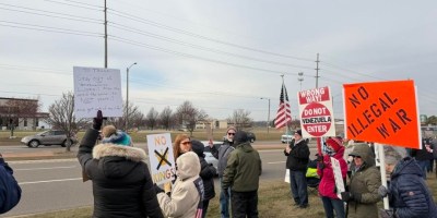 Grupo de personas con carteles protesta pacíficamente en un centro comercial de Bloomington contra la intervención de Estados Unidos en Venezuela.