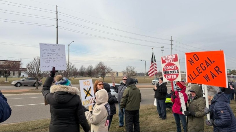 Grupo de personas con carteles protesta pacíficamente en un centro comercial de Bloomington contra la intervención de Estados Unidos en Venezuela.