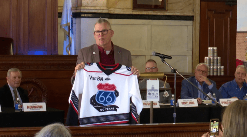 Un hombre sostiene la camiseta de los Bison de Bloomington conmemorativa al centenario de la ruta 66.